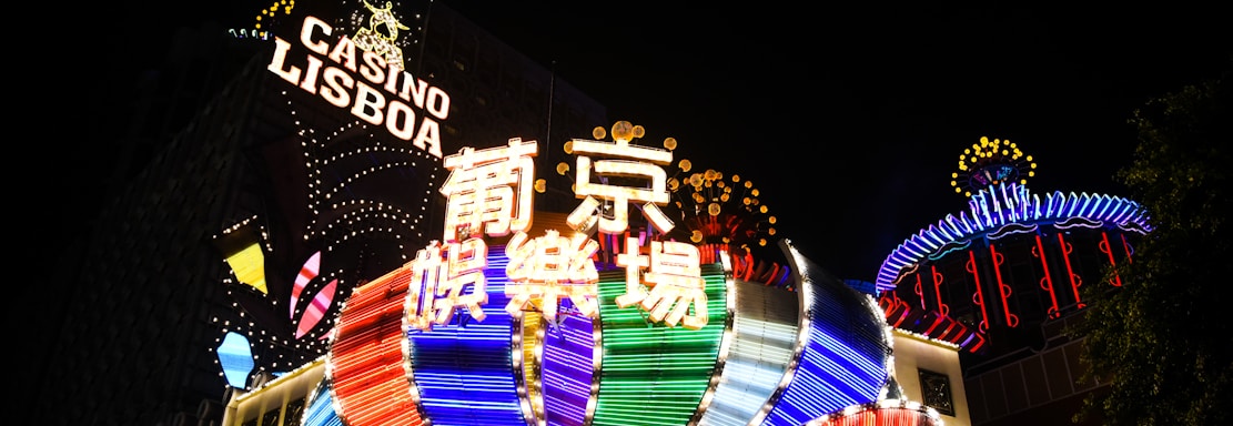Bright neon signs in multiple colors illuminate the night, prominently displaying the name 'Casino Lisboa' alongside signage in Chinese characters. The lights form intricate patterns and vibrant displays, creating a lively and energetic atmosphere.